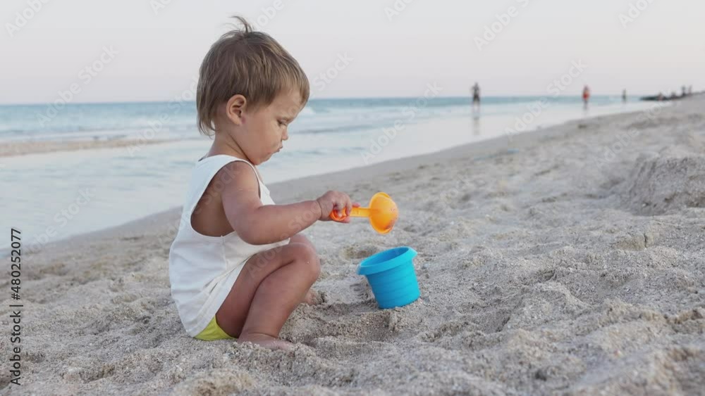 Boy playing with toys on the beach building beads and turrets smiling at someone behind the scenes on summer vacation Boy playing with toys on the beach building beads and turrets smiling at someone behind the scenes on summer vacation