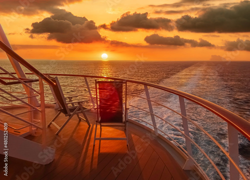  Vue de deux chaises longues sur le pont d'un navire de croisière au coucher de soleil dans le sillage du navire de croisière. Vue depuis la poupe du navire. 