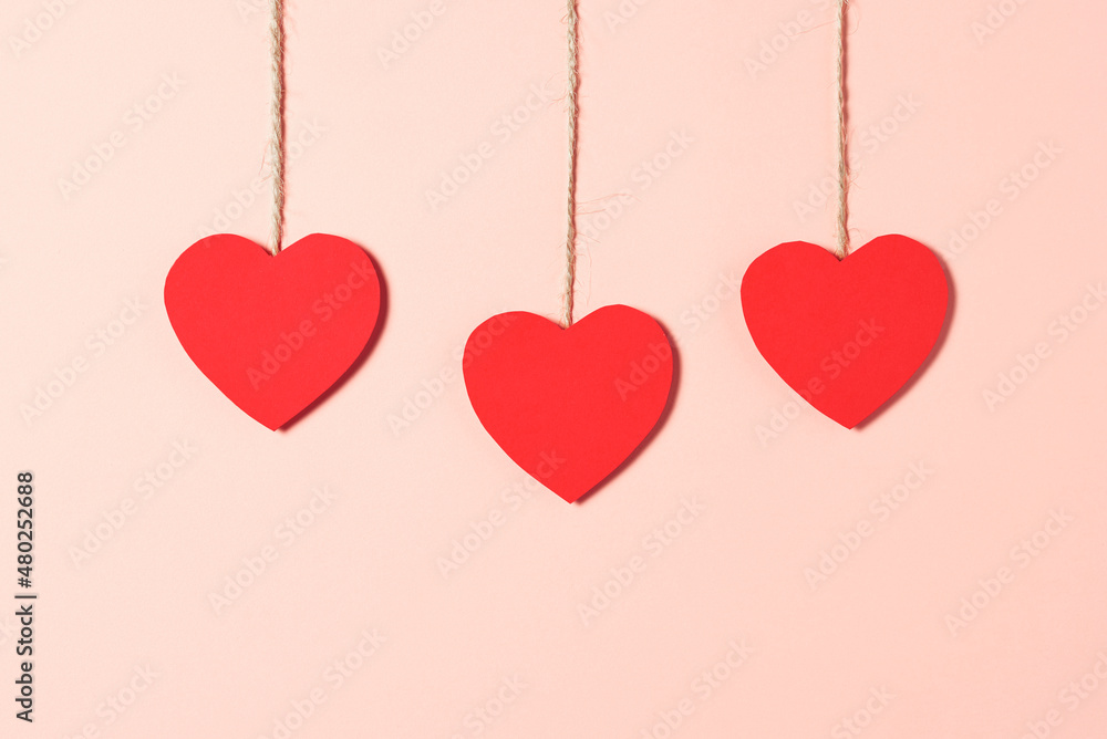 bright red heart-shaped cards hanging on a rope on a peach paper background