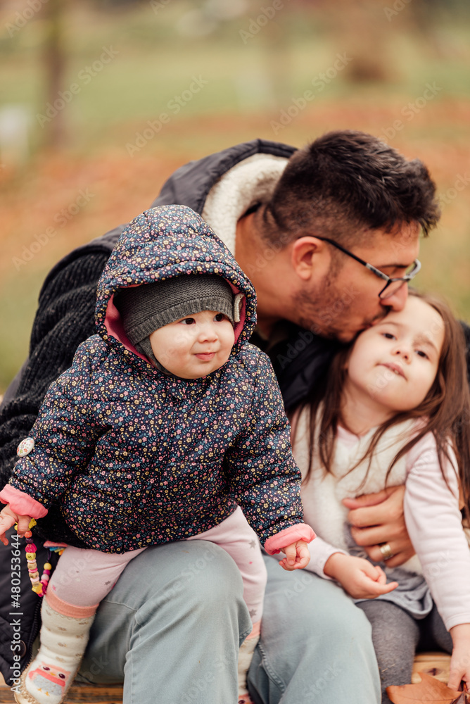 A single father with two daughters sitting on a bench in the park A single father with two daughters sitting on a bench in the park