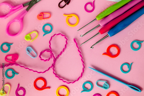 Bright crochet tools on a pink background. Crochet hooks, colored markers, needle and scissors. photo