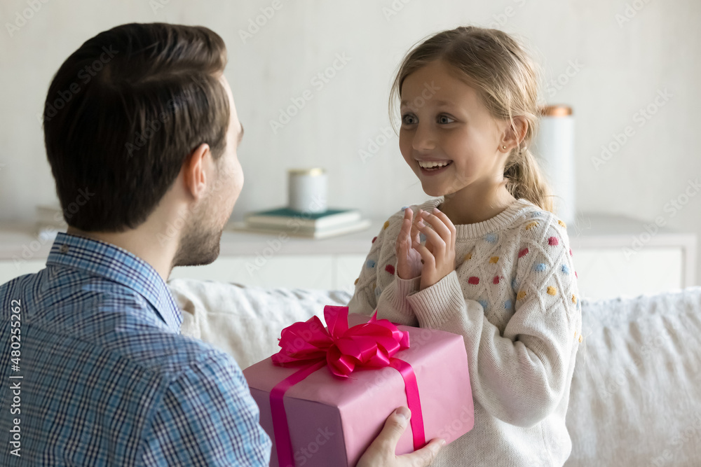Surprised cheerful adorable little kid girl looking at father, feeling excited of getting wrapped gift box, listening best wishes or congratulations with happy birthday, celebrating together at home. Surprised cheerful adorable little kid girl looking at father, feeling excited of getting wrapped gift box, listening best wishes or congratulations with happy birthday, celebrating together at home.