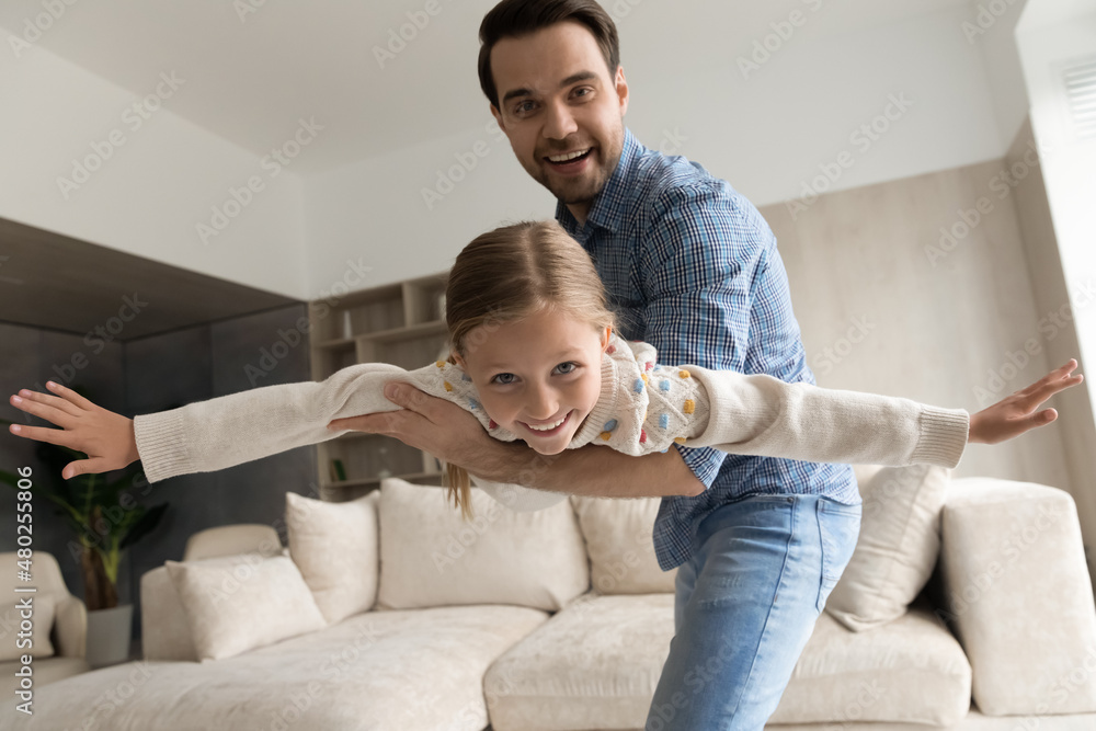 Portrait of happy caring young dad holding in hands flying joyful adorable laughing child daughter, enjoying domestic entertaining weekend activity, playing games at home, good relations concept. Portrait of happy caring young dad holding in hands flying joyful adorable laughing child daughter, enjoying domestic entertaining weekend activity, playing games at home, good relations concept.