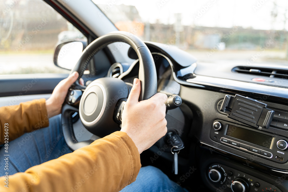 Caucasian or eastern ethnicity man casually dressed with hands holding driving wheel in car on sunny autumn, winter or spring day. No face, anonymous, travel, exam, lesson, learning, taxi driver