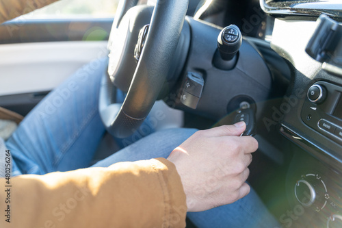 Young eastern man casually dressed with hands holding driving wheel, starting engine turning on ignition key in car on sunny day. No face, anonymous, travel, exam, lesson, learning, taxi driver