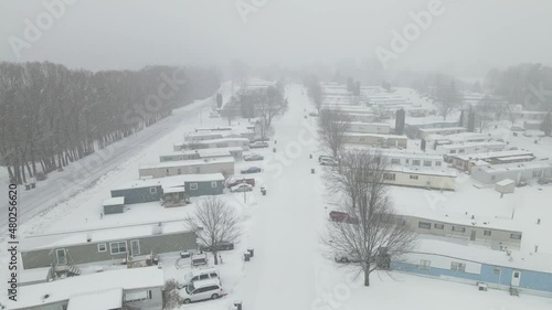 Drone view over mobile home park in winter. Snowing falling fast and covering the ground. Low visibility. Mountain and forest snow covered. 