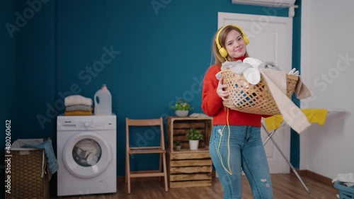 Young blonde woman listening to music throwing clothes out of basket at laundry room photo