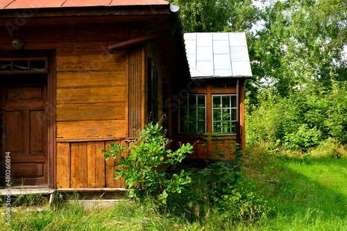 A close up on an old abandoned wooden house located in the middle of a forest or moor next to some trees, a well and a fence, spotted on a sunny summer day during a hike on a Polish countryside