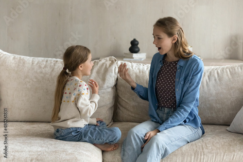 Slika na platnu Happy small Z generation child girl learning pronouncing sounds correctly with caring mother, sitting together on couch at home