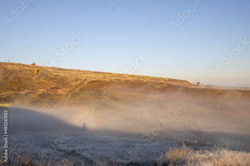 Autumn landscape in the early morning. Fog-covered expanses through which the first rays of the rising sun pass. Trees and hills in the fog. Dawn on a cold autumn morning.