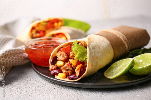 Plate of tasty Mexican burrito with vegetables and sauce on grey background