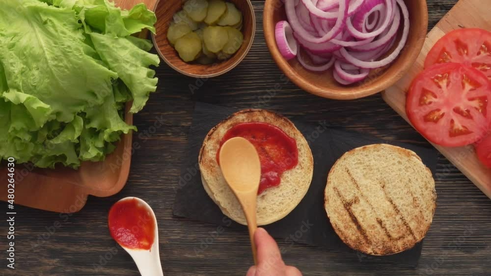 Top view of the wooden spoon spreading a tomato sauce on the burger bun Top view of the wooden spoon spreading a tomato sauce on the burger bun
