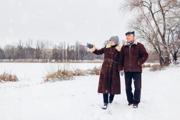 Senior family couple walking outdoors during snowy winter weather. Elderly people holding hands. Valentine's day