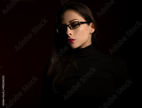 Business thinking woman in fashion eye glasses looking down in black clothing on dark shadow red background. Closeup profile
