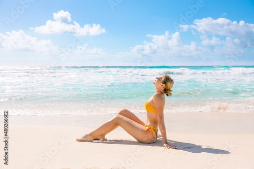 Young slim woman in bikini lying on tropical beach sunbathing under summer sun