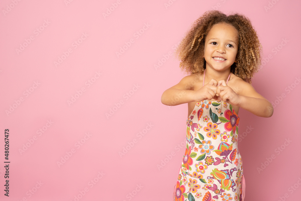 Beautiful cute little girl making heart figure with fingers standing isolated over pink background. Beautiful cute little girl making heart figure with fingers standing isolated over pink background.
