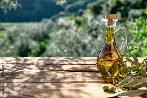 Fotografie, Obraz Extra virgin olive oil and olive branch in the bottle on wooden table in the olive grove