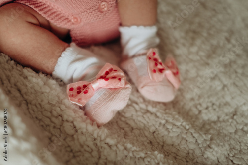 Legs of a newborn girl in pink socks with bows. The child lies in the crib
