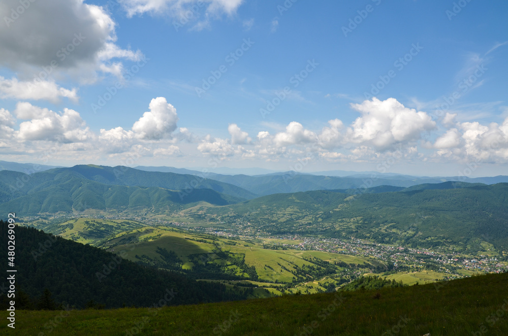 Beautiful mountain landscape with green forests, hills, meadow and village in the valley. Carpathian Mountains, Ukraine