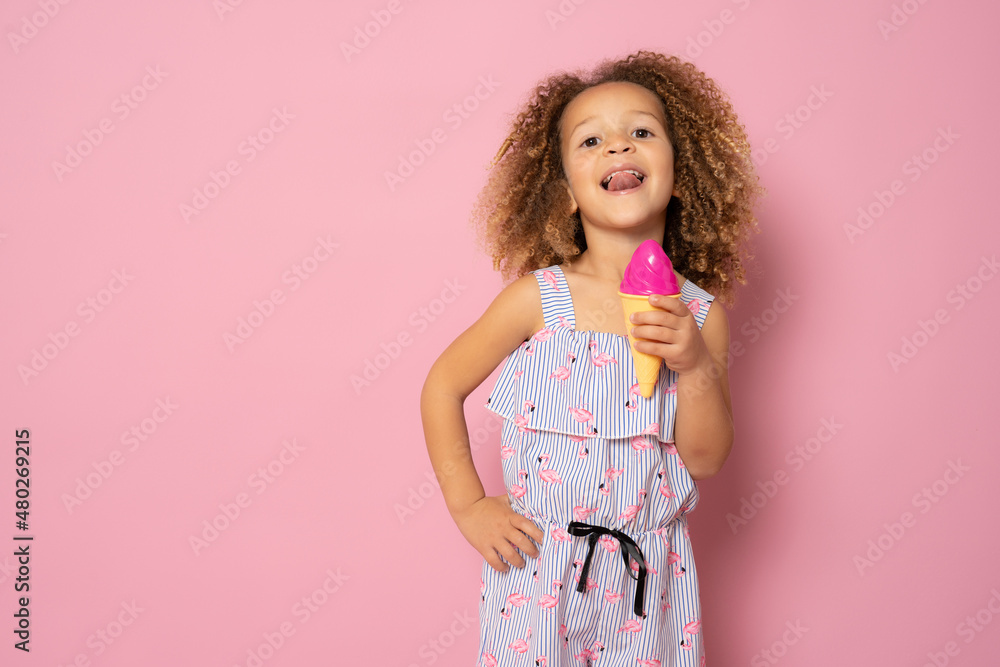 Cute little girl with curly hair holding ice cream standing isolated over pink background. Cute little girl with curly hair holding ice cream standing isolated over pink background.
