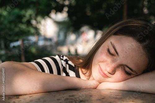 Portrait of a young lovely woman with blue eyes and freckles in a striped T-shirt and jeans sits on chair and enjoying sun.