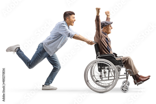 Full length profile shot of a young man running and pushing a happy elderly man in a wheelchair