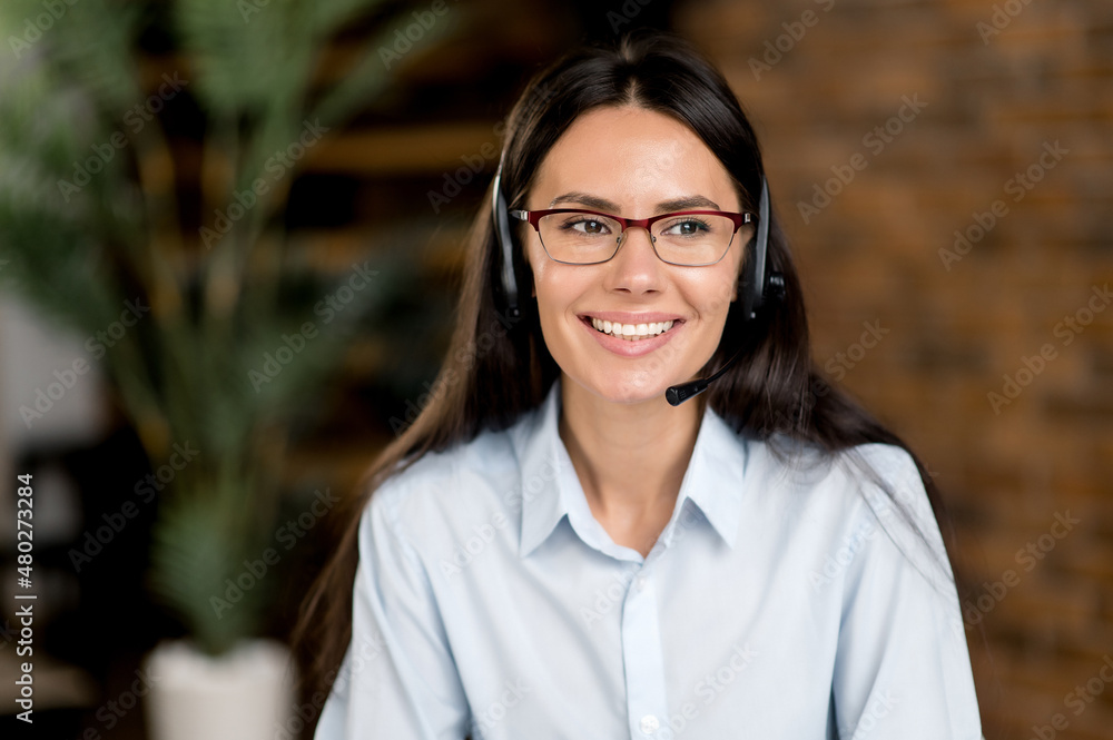 Pleasant attractive young adult caucasian brunette woman wearing headset and glasses, freelance worker, call center employee, hot line operator, in formal shirt, looking to the side, smiles friendly Pleasant attractive young adult caucasian brunette woman wearing headset and glasses, freelance worker, call center employee, hot line operator, in formal shirt, looking to the side, smiles friendly