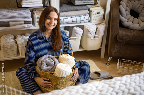 Portrait of happy young domestic woman in pajamas posing with straw basket for linens storage photo