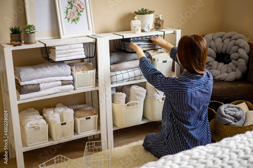 Domestic woman in pajamas neatly putting folded linens into cupboard vertical storage Marie Kondo photo