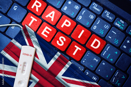 COVID-19 positive antigen rapid test kit on face mask with British flag on computer keyboard. Concept of home use Covid self testing in UK. photo