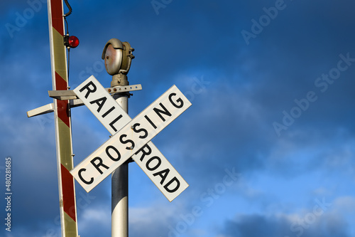 A railroad crossing sign with the barrier in the raised position against moody blue sky.  The evening sunlight highlights the text in the words