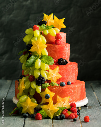 Three teir Cake that resembles a wedding cake made out of watermelon and assorted fruits cascading down the side of cake photo