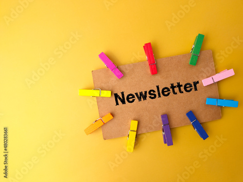 Colored wooden clips and brown card written with text Newsletter on yellow background. photo