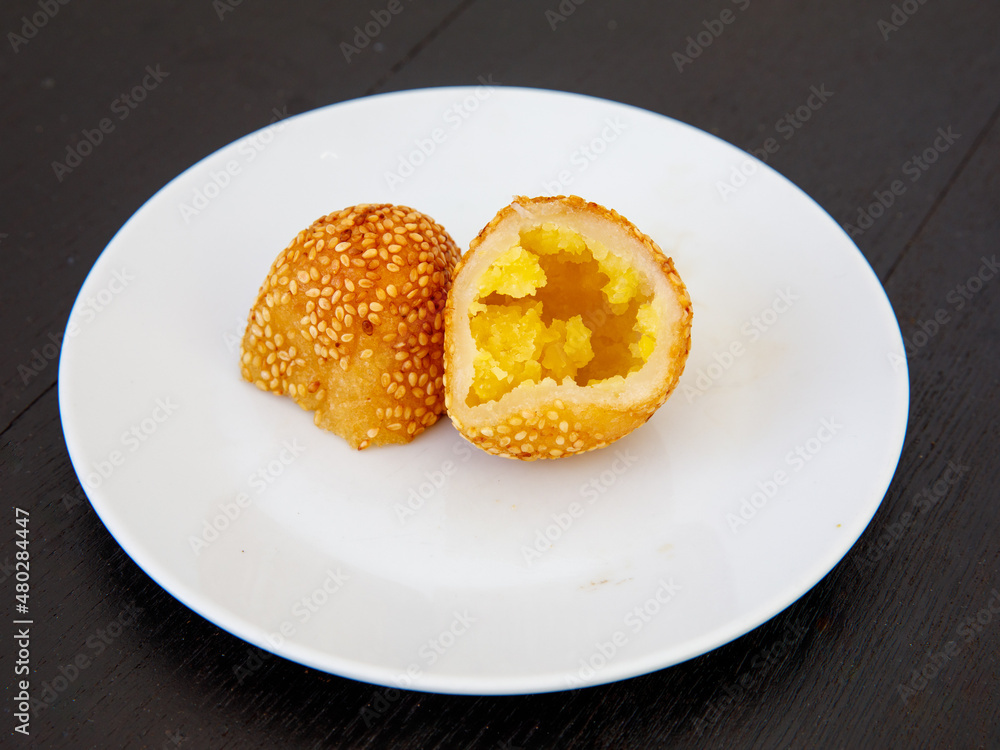 Khanom Kai Hong with sesame or Swan Eggs Dessert, native Thailand fried dessert balls like doughnuts with yellow bean paste on white plate on black wooden background Khanom Kai Hong with sesame or Swan Eggs Dessert, native Thailand fried dessert balls like doughnuts with yellow bean paste on white plate on black wooden background