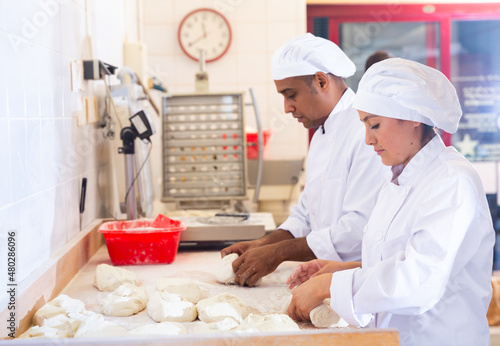 Latin american female baker engaged in breadmaking, forming bread loaves from raw dough
