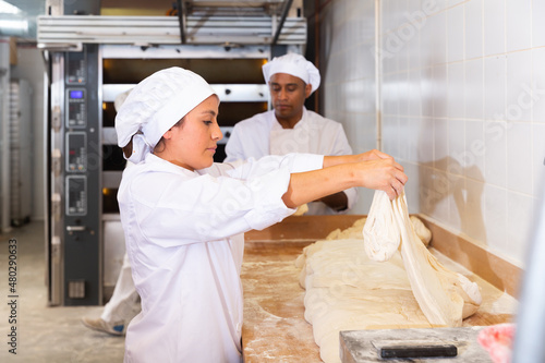 Latin american woman working in bakehouse, kneading dough for baking bread