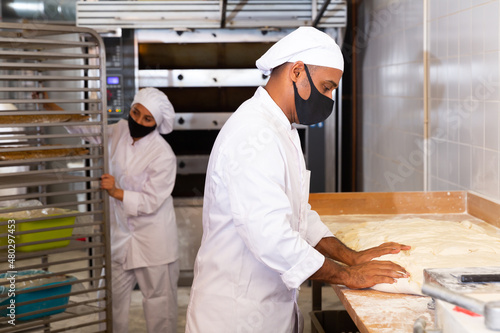 Portrait of confident professional Hispanic baker working with raw yeasted dough in bakery