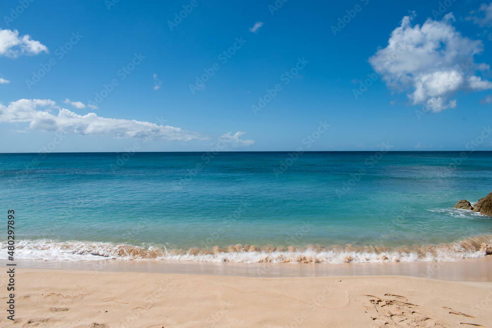 A view from the sand of a beach on the island of Barbados in the Caribbean with clean, blue water. Image is great for postcards.