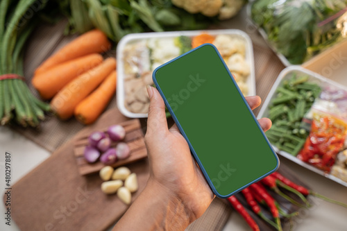 Hands holding a smartphone with a vegetable background