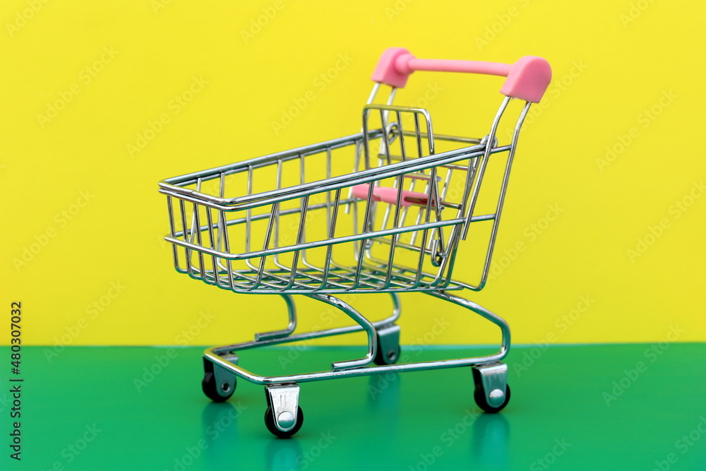 A miniature shopping cart stands on a green and yellow background. A miniature shopping cart stands on a green and yellow background.