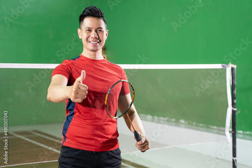Smiling male badminton player holding racket with thumbs up gesture © Odua Images