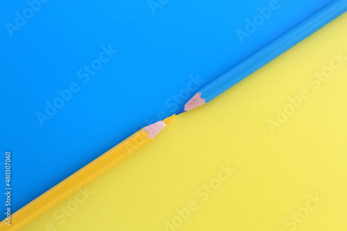 On a blue and yellow background, two pencils of the same color lie at the same time with space for text.