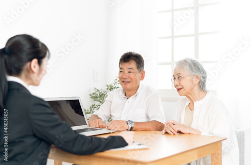 パソコンで説明するスーツ姿の女性と高齢者夫婦 