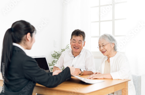 パソコンで説明するスーツ姿の女性と高齢者夫婦 