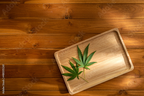 Photo of cannabis leaves in a wooden tray on a wooden table with warm light and shadow background. Copy space Decoration for backdrop artwork design or Banner. Eatable vegetable nature concept ideas