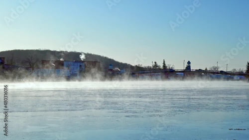 Sheets of ice and mist form on a moving river as it passes through a small town. photo