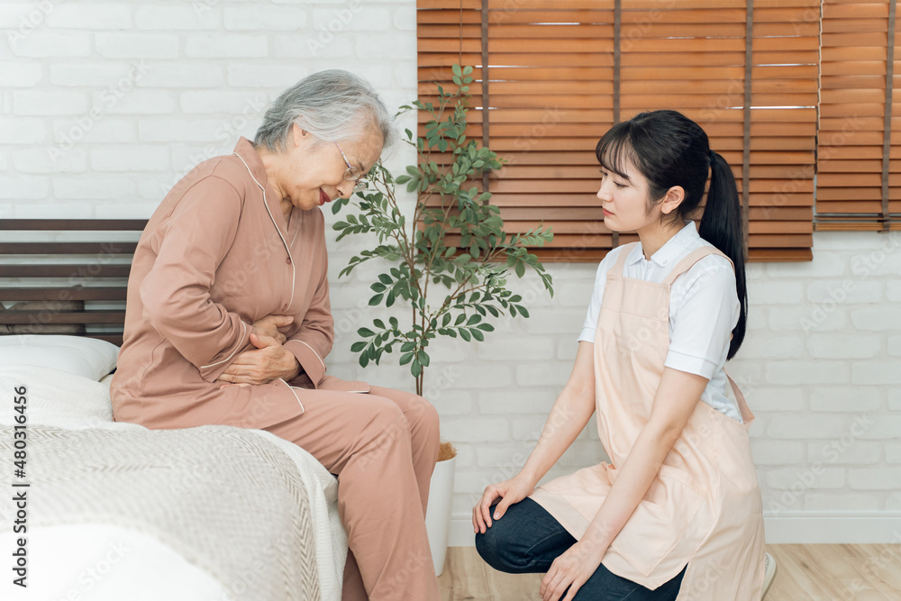 Obraz premium 痛がる高齢者女性と介護士の女性（腹痛）