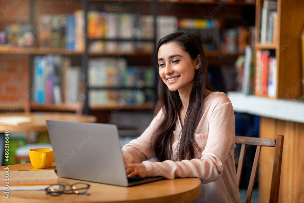 Remote learning and online work concept. Happy arab woman using laptop computer at cozy urban cafe, free space Remote learning and online work concept. Happy arab woman using laptop computer at cozy urban cafe, free space