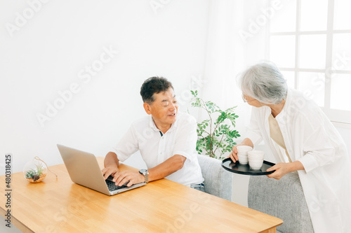 パソコンを使う高齢者男性とお茶を運ぶ女性 