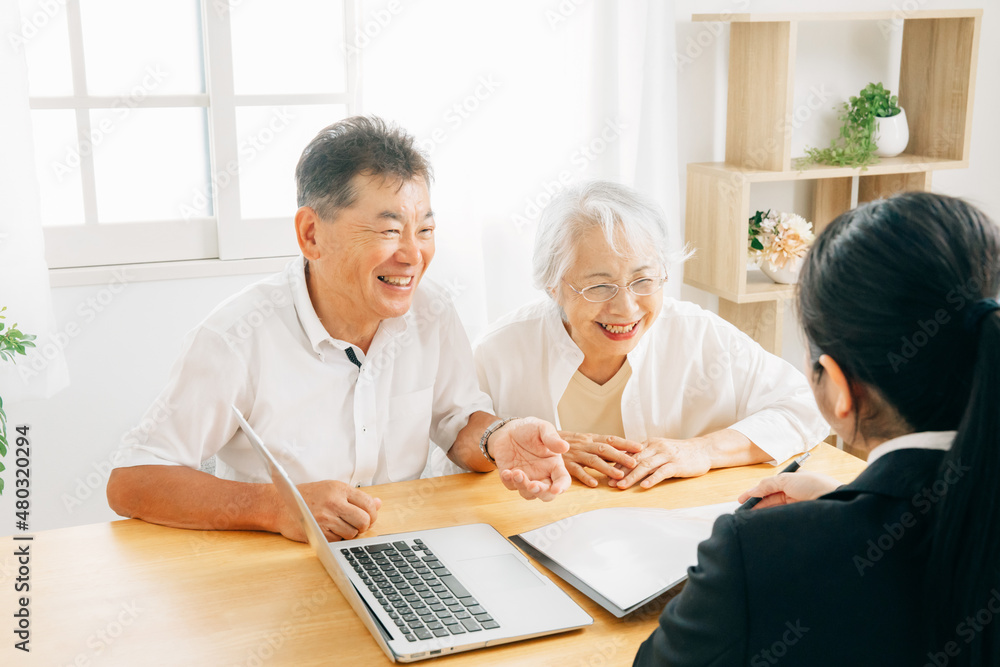パソコンで説明するスーツ姿の女性と高齢者夫婦
